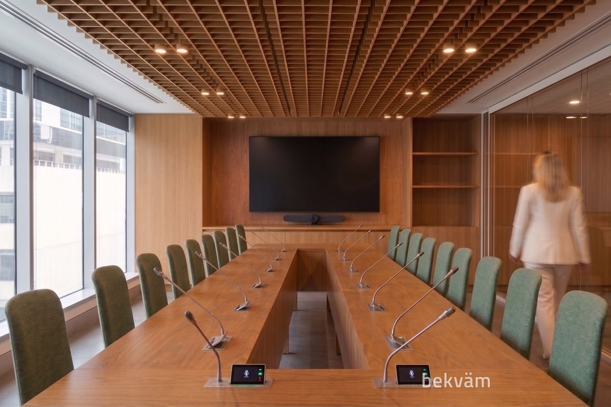 Sala de diretoria com mesa longa, microfones e tela